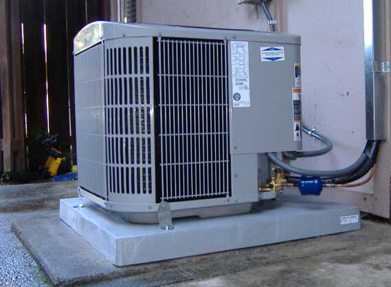 Air conditioning unit installed on concrete base, featuring metal grille and connecting pipes.
