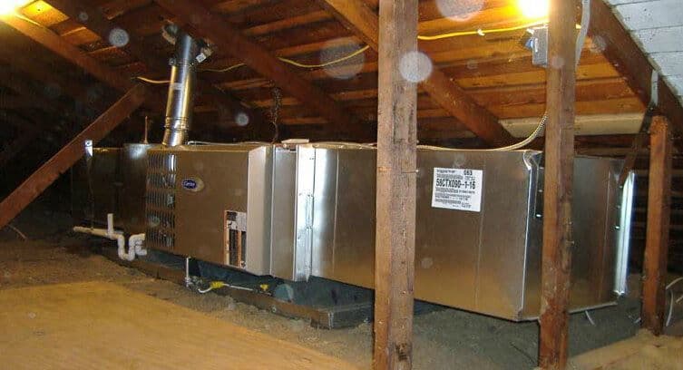 HVAC system installed in an attic with wooden rafters and insulation.