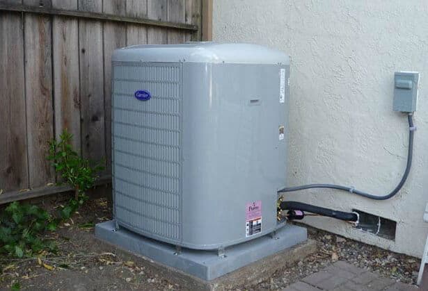 Gray air conditioning unit installed outside a home beside a wooden fence.