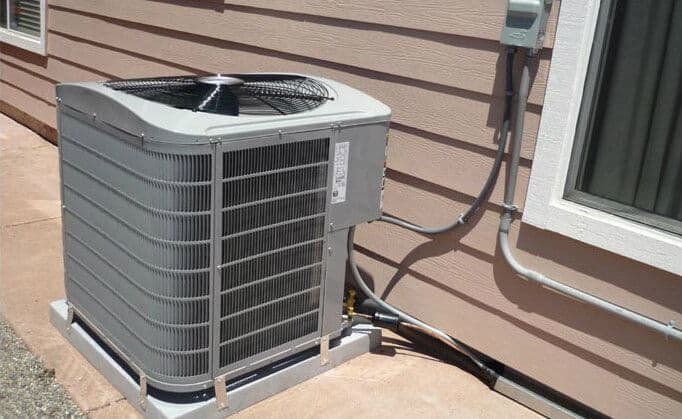 Air conditioning unit installed outside a house along a beige wall.