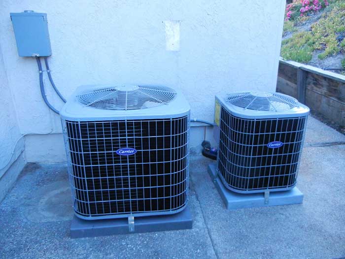 Two Carrier air conditioning units installed beside a building on a concrete surface.