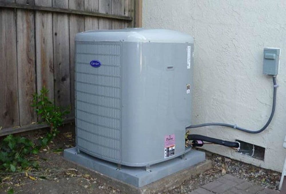 Gray air conditioning unit installed outside a house near a wooden fence.